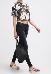 Avkortad svart blommig topp med gula och vita blommor, kombinerad med svarta jeans. Svart dragsko-väska och bruna sandaler med glidsula och silverdetaljer.