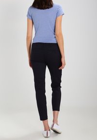 Mörkblå smala byxor med en mid-rise passform, parat med en ljusblå åtsittande skjorta och vita slip-on skor med röda och mörkblå ränder.