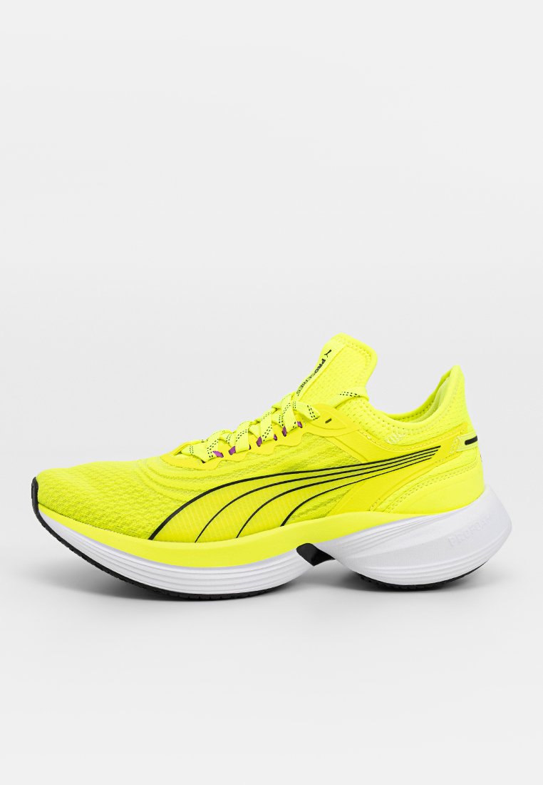 Helle gelbe Lauf sneakers mit schwarzen Streifen, dicker weißer Sohle und Obermaterial aus Netz, gezeigt im rechten Seitenprofil auf einfarbigem Hintergrund.