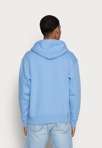 Ljusblå hoodie med en rymlig huva, ribbade ärmslut och nederkant, tillverkad av mjukt material. Har en avslappnad passform med minimala sömnadsdetaljer.