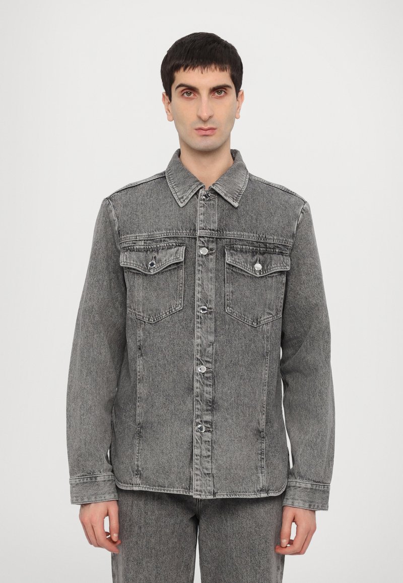 Grå denimjakke med knappelukking foran, to brystlommer og klassisk krage. Har en litt falmet finish og myk tekstur.