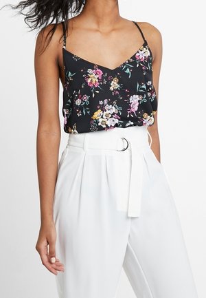 Black floral camisole with thin straps, featuring colorful flowers against a dark background. Paired with high-waisted white trousers and a belt.