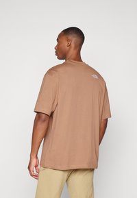 T-shirt en coton marron avec un col rond et des manches courtes. Présente un petit logo brodé sur le haut du dos.