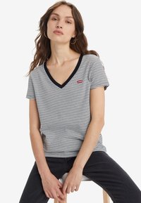 Randig kortärmad t-shirt i svart och vitt med V-halsringning, med en liten röd Levi's-logotyp på vänster bröst. Tillverkad av bomull.