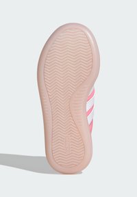 Podešev růžového tenisky s texturovaným gumovým dnem, které má vzor rybí kosti a bílé tři pruhy na boku.