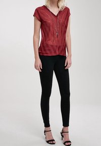 Top rojo de manga corta con estampado y escote en V, combinado con pantalones negros ajustados y sandalias de tacón alto. Destaca un largo collar de plata.