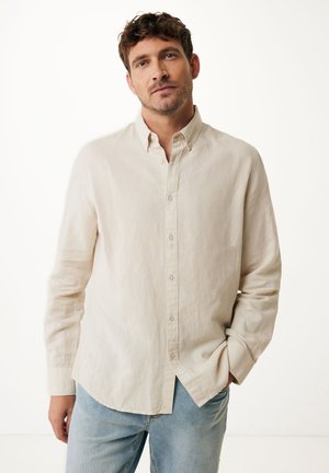 Camicia button-up beige chiaro in lino, con colletto tradizionale, maniche lunghe e orlo leggermente arrotondato, abbinata a jeans blu chiaro.