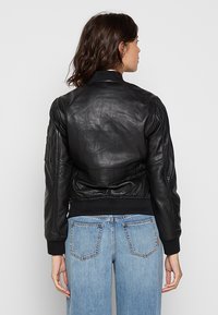 Veste bomber en cuir noir avec des poignets et un ourlet côtelés, présentant une texture lisse, des coutures subtiles et un détail de poche latérale.