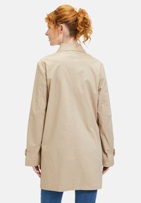 Beige Trenchcoat mit geradem Schnitt, langen Ärmeln und Knopfdetails an den Manschetten. Leichte Textur und minimalistisches Design.