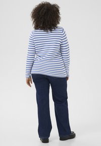 Blue and white striped long-sleeve top paired with dark blue flared jeans, featuring a straight back and textured fabric. Black footwear visible.