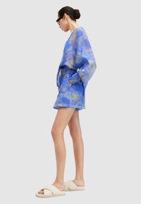 Tops s plavim i žutim tie-dye uzorkom, dugim rukavima i opuštenim krojem, uz kratke hlače s elastičnim pojasom. Upareno s bež debelim sandalama.