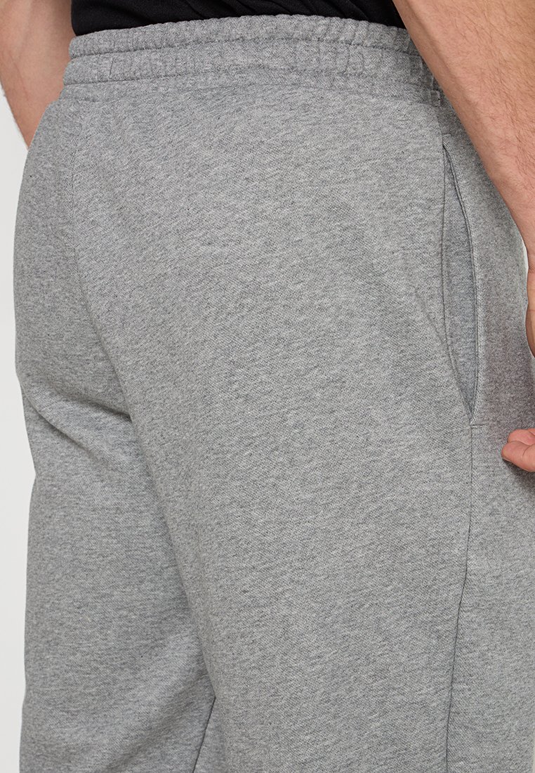 Pantalon de jogging gris en mélange de coton, avec une taille élastique et des poches latérales. La texture semble douce et légèrement brossée.