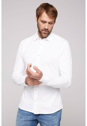 Witte overhemd met lange mouwen, een button-down kraag en een voorste knoopsluiting, gecombineerd met lichtblauwe jeans; gladde stof en een getailleerd ontwerp.