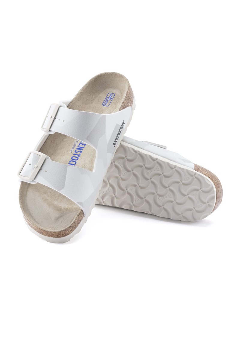Vita Birkenstock-sandaler har en slät ovansida med två justerbara remmar och en formad fotbädd av kork. Den strukturerade sulan ger bra grepp.