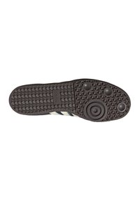 Suola di una scarpa Adidas marrone con grip testurizzato, motivi circolari e tre punti neri su uno sfondo bianco.