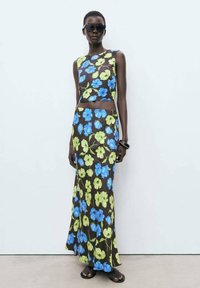 Bloemen crop top en maxi rok set in donkerbruin, met blauwe en groene bloemen. Glad materiaal, aansluitend ontwerp, gecombineerd met zwarte sandalen.