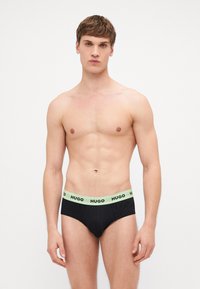 Boxers noirs avec une ceinture élastique vert clair comportant le logo « HUGO » en texte noir. Le tissu semble lisse avec un ajustement près du corps.
