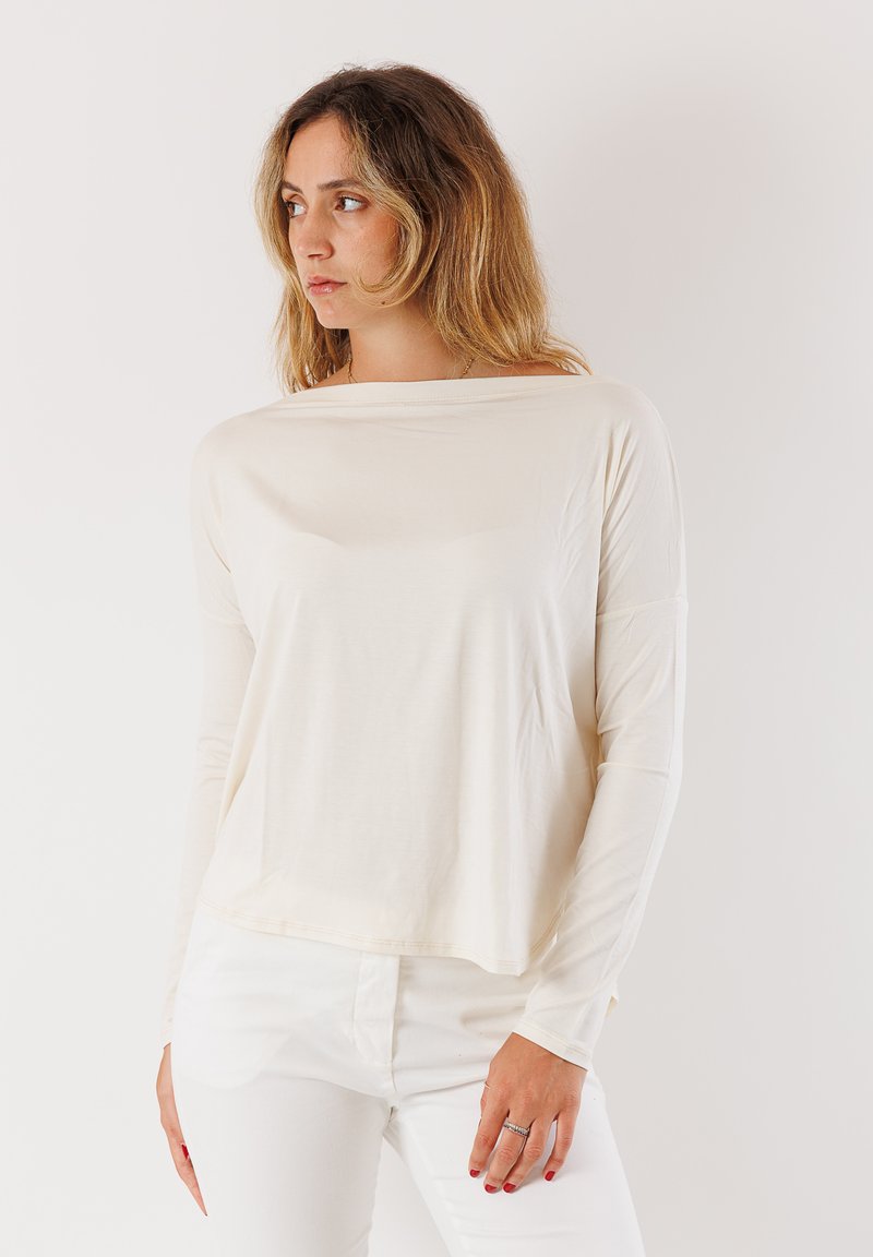 Top a maniche lunghe di un leggero beige con una vestibilità rilassata e scollatura ampia. Realizzato in tessuto morbido con una caduta delicata. Abbinato a pantaloni bianchi.