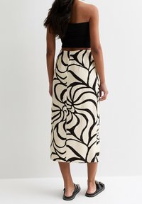 Maxi rok in crème met gedurfd zwart bloemenpatroon. Lichtgewicht stof, A-lijn silhoët en zijsplit detail. Zwarte sandalen complementeren het ontwerp.
