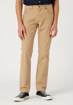 Pantalones de lienzo de algodón beige con un ajuste de pierna recta, que cuentan con presillas para cinturón, bolsillos frontales y zapatillas negras de caña baja.