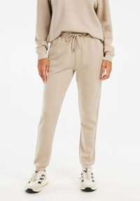 Beige Jogginghosen mit elastischem Bund und Kordelzug. Hergestellt aus weichem Material, mit seitlichen Taschen und einem schmal zulaufenden Bein-Design.
