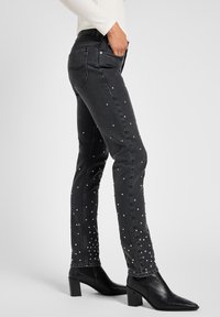 Calças de ganga skinny pretas com tachas prateadas ao longo das pernas, apresentando um design clássico de cinco bolsos e uma cintura ajustada.