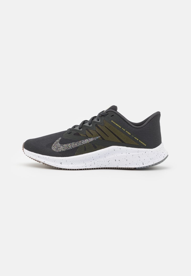 Chaussure de course gris foncé avec une semelle blanche tachetée, un swoosh Nike pailleté multicolore et un texte jaune sur le côté indiquant "Engineered for Speed."