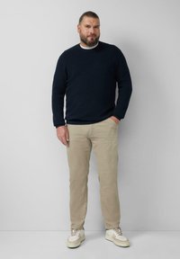 Marine gebreide trui, lichtbeige broek en witte sneakers met beige accenten, staande tegen een effen achtergrond.