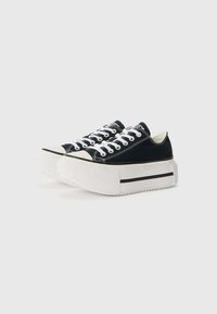 Black canvas sneakers featuring a thick white platform sole, white laces, and subtle black accents at the base. Rounded toe design.