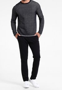 Pull en tricot noir à manches longues avec un motif texturé, associé à un pantalon noir et des baskets blanches, doté d'un col rond et d'une coupe ajustée.