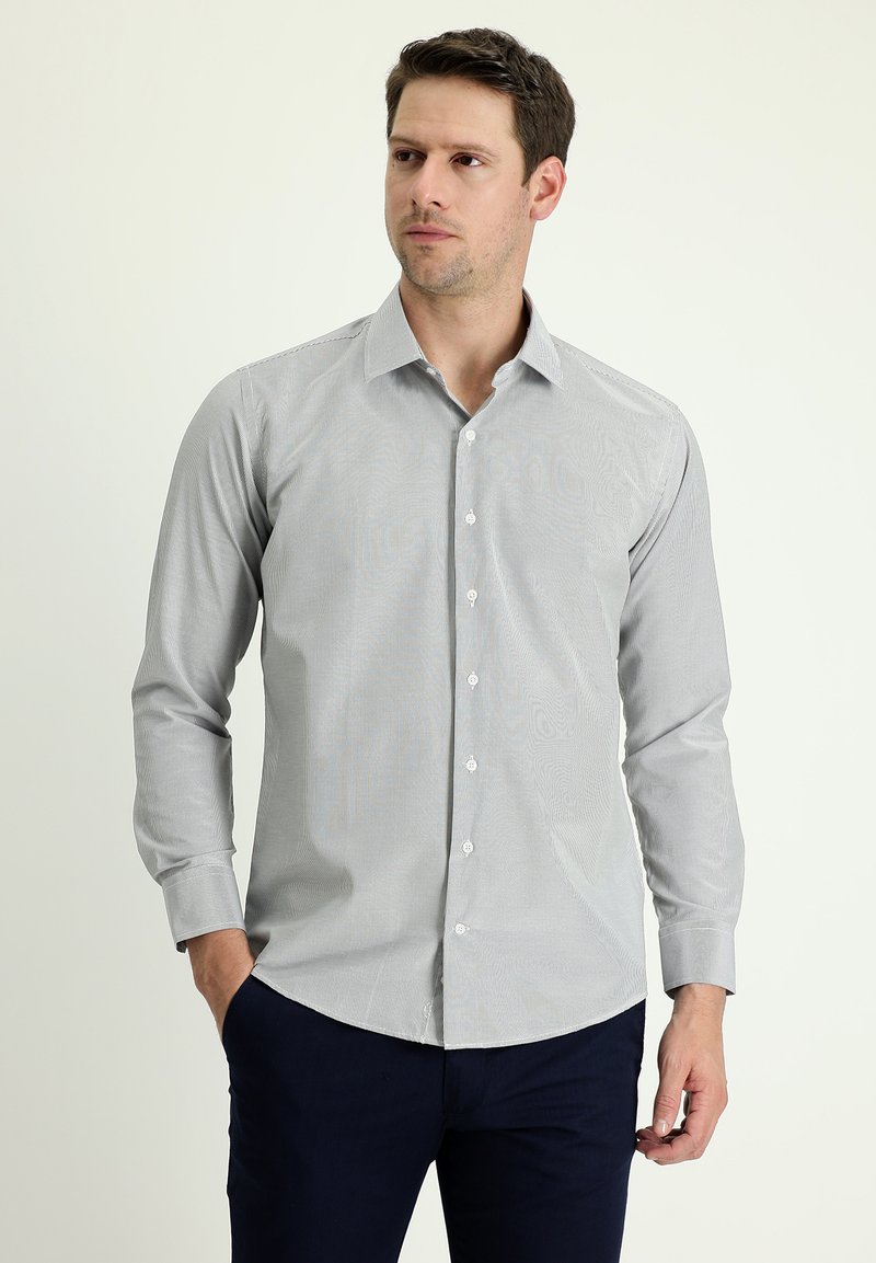 Camicia grigia chiaro con un sottile motivo a righe, maniche lunghe e colletto a punta, abbinata a pantaloni blu navy scuri.