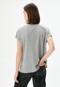 Lysegrå t-shirt med korte ærmer og opfoldede ærmer, afslappet pasform og en subtil syning detail bagpå. Bærer med sorte cargo bukser.