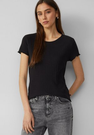 T-shirt noir à côtes avec des manches courtes effilochées ; col rond ; design ajusté, associé à un jean gris taille haute. Branding minimal sur le jean.