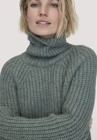 Strick-Turtleneck-Pullover aus einem weichen, strukturierten Tealfaden, mit lockerer Passform und Rippdetails am Kragen und den Ärmelbündchen.