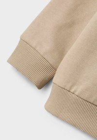 Maniche di felpa beige con texture a coste. Tessuto morbido e liscio con un design aderente, che presenta un'estetica pulita e minimale.