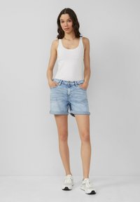Lichtblauwe denimshorts met opgerolde zoom, voorzakken en een mid-rise pasvorm, gecombineerd met een witte tanktop en witte sneakers.
