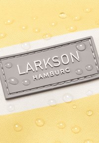 Logo Larkson Hamburg na szarej łatce przyszytej do materiału w żółto-białe paski, z kroplami wody na powierzchni.