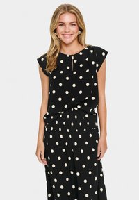 Haut noir à pois avec des manches courtes et un détail en forme de trou de serrure au niveau du col, fabriqué à partir d'un tissu léger, associé à une jupe à motifs assortie.