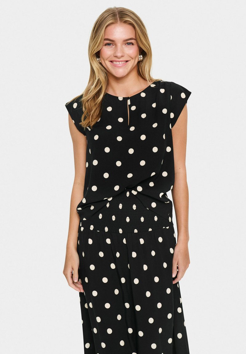 Haut noir à pois avec des manches courtes et un détail en forme de trou de serrure au niveau du col, fabriqué à partir d'un tissu léger, associé à une jupe à motifs assortie.