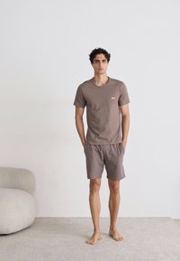 T-shirt à manches courtes marron et shorts assortis, tous deux en tissu doux. Le T-shirt arbore un petit logo sur la poitrine.