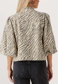 Giacca a strisce zebrate beige e grigia con maniche a palloncino, vista da dietro. Abbinata a jeans neri, con dettagli minimi.