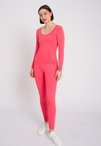 Maglia a maniche lunghe attillata e leggings di un vivace rosa. Tessuto liscio e elasticizzato con una sottile trama a coste, abbinato a sneakers bianche.