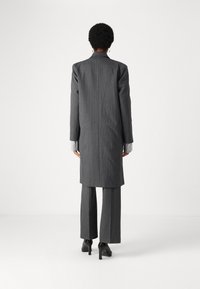 Completo grigio a righe sottili con giacca lunga e pantaloni su misura, con polsini in maglia testurizzata. Abbinato a scarpe nere con tacco alto.