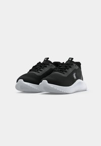 Um par de sapatos de atletismo Calvin Klein pretos com solas brancas, design com atacadores e logo em destaque nas laterais e na língua, sobre um fundo simples.