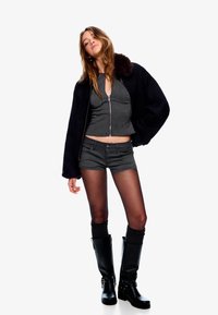 Top gri scurt cu fermoar argintiu, pantaloni șort gri, cizme negre până la genunchi și o jachetă neagră cu guler de blană. Textură netedă pe întreaga suprafață.