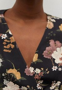 Vestido envolvente floral con escote en V profundo, fondo negro, flores multicolores vibrantes y una textura de tela suave y ligera.