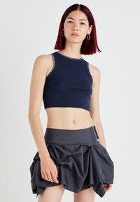 Top cropped em azul marinho com nervuras e costura branca contrastante, emparelhado com uma saia multi-camada texturizada em cinza escuro, apresentando um detalhe de fivela lateral.