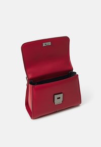 Raudona odinė rankinė stačiakampio formos, su sidabriniu užsegimu ir lygia tekstūra. Viduje yra užtrauktuko kišenė.