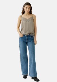 Graues Seiden-Camisole mit Spitzenbesatz und Spaghetti-Trägern, kombiniert mit hellblauen, ausgestellten Jeans und schwarzen Stiefeletten.