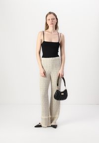 Svart tettsittende tanktopp med tynne stropper, vide beige teksturerte bukser med frynset hem, svart kviltet håndveske og spisse svarte flater.